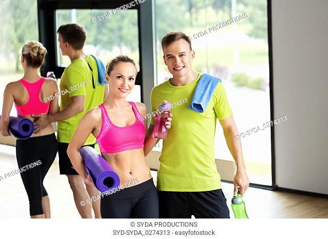 couple with bottles, exercise mat and towel in gym