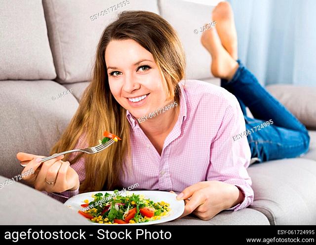 Young woman eating tasty greenery salad at home
