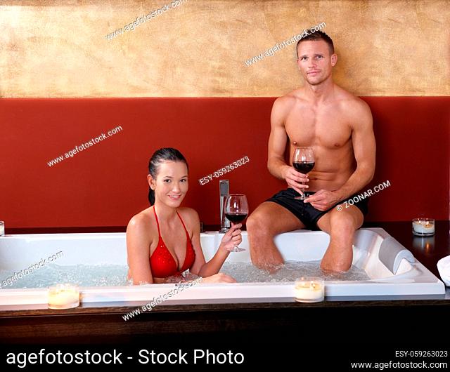 Portrait of happy couple having wine in jacuzzi, smiling at camera