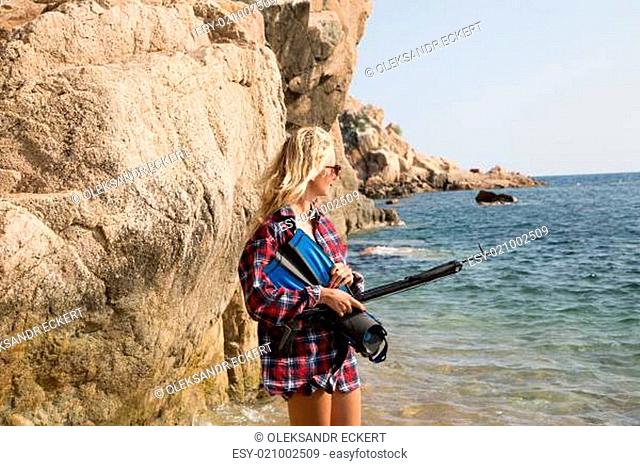 Girl with harpoon in flannel shirt on the rocky beach