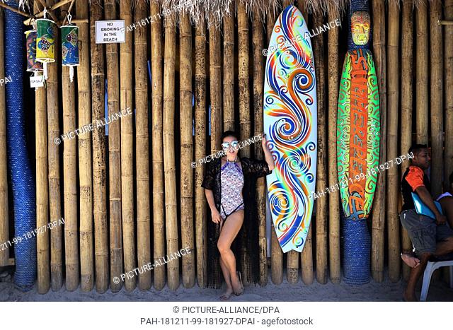 10 December 2018, Philippines, Boracay: A girl poses in a beach bar next to a surfboard. The beaches of the island of Boracay were closed to the public for six...