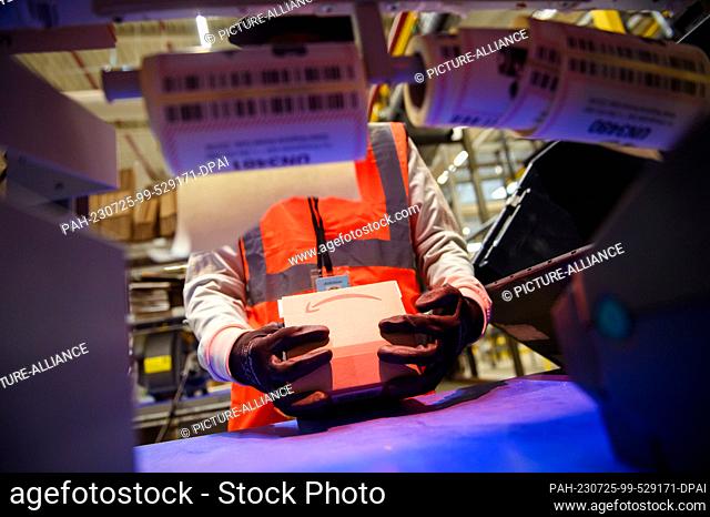 25 July 2023, Lower Saxony, Winsen (Luhe): An employee uses a scanner to pack goods into a suitable shipping package at the Amazon Logistik GmbH logistics...