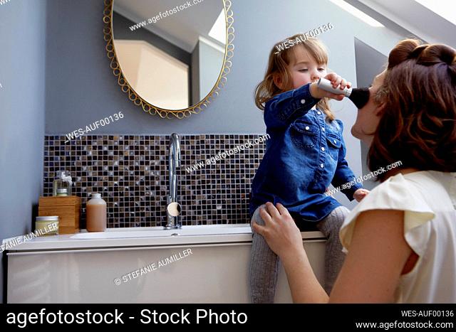 Toddler girl applying rouge on her mother's face in bathroom
