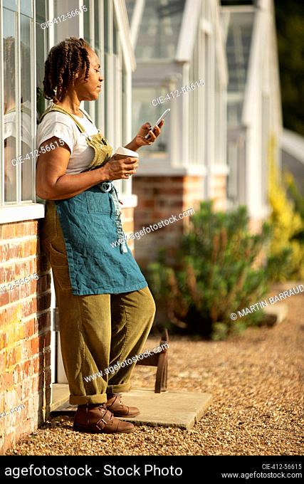 Female garden center owner enjoying coffee break at sunny greenhouse