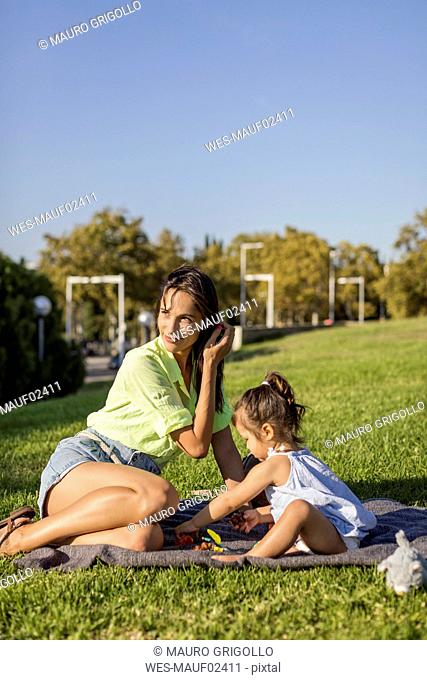 Happy mother playing with daughter on a blanket in park