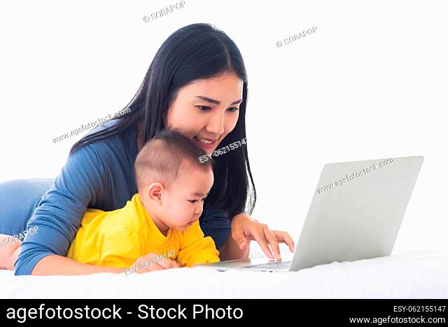 Asian happy young mother and baby lifestyle working on laptop, woman mom and daughter reading and learning technology on screen while notebook computer on...
