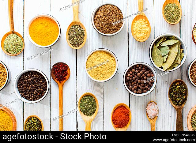 Assorted colorful organic spices and herbs in ceramic bowls and wooden spoons on white background. Tasteful and healthy cooking concept