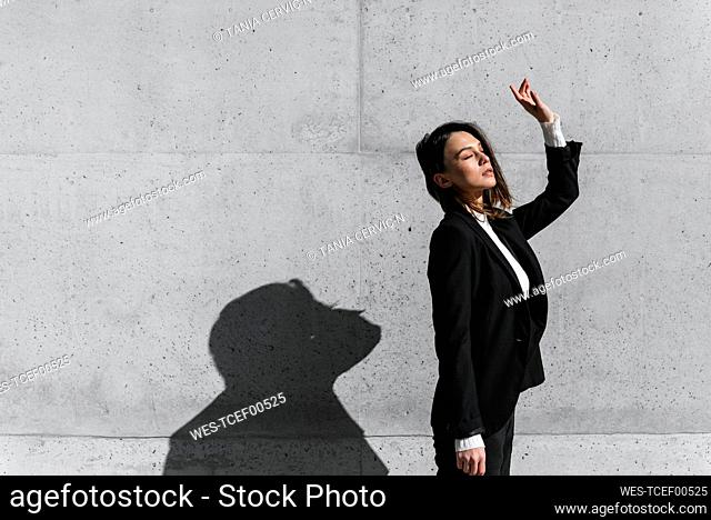 Young woman wearing black suit standing in front of concrete wall