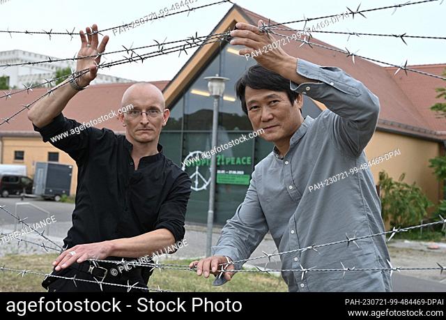 21 July 2023, Brandenburg, Potsdam: The curators Frederic Krauke (l) and Jooman Cha look through a barbed wire fence before the press preview of the exhibition...