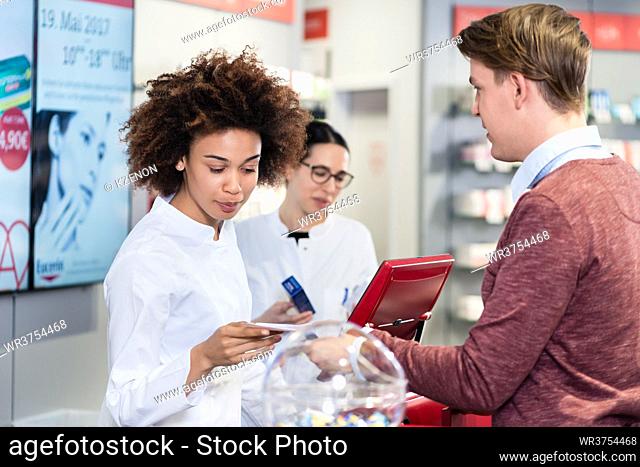 Dedicated female pharmacist checking a medical prescription while selling prescribed medicines to a young male customer in a modern drugstore