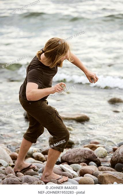 Young man throwing stones on beach, Gotland, Sweden
