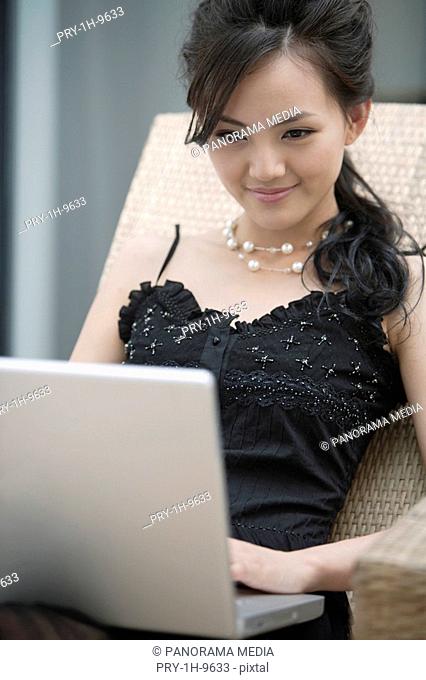 Young woman sitting on wicker chair using laptop