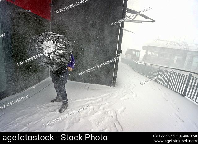 27 September 2022, Bavaria, Oberstdorf: An excursionist tries to protect himself from the strong wind in the driving snow at the Fellhorn cable car's middle...