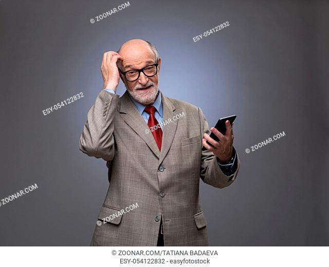 Portrait of funny senior man with phone scratching his head, gray copy space