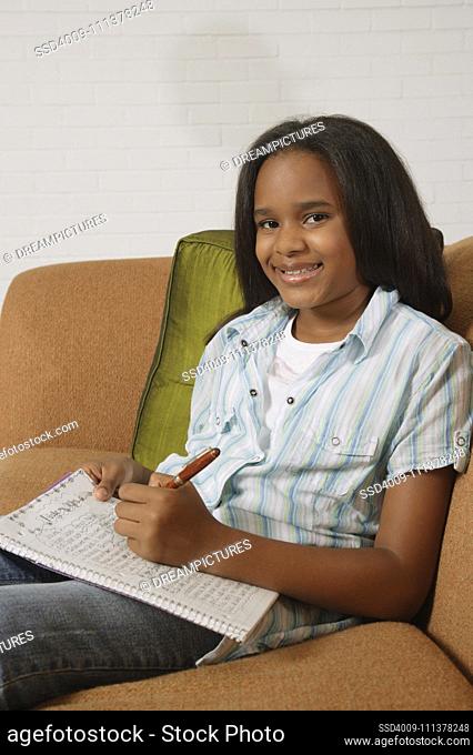 African girl writing in notebook on sofa