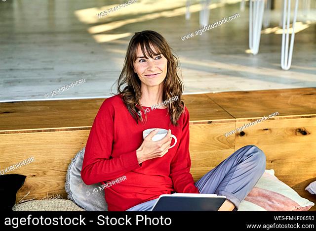 Smiling woman holding coffee cup while using digital tablet at home