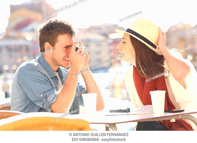 Side view of a tourist joking and photographing his girlfriend in a hotel terrace during summer holidays