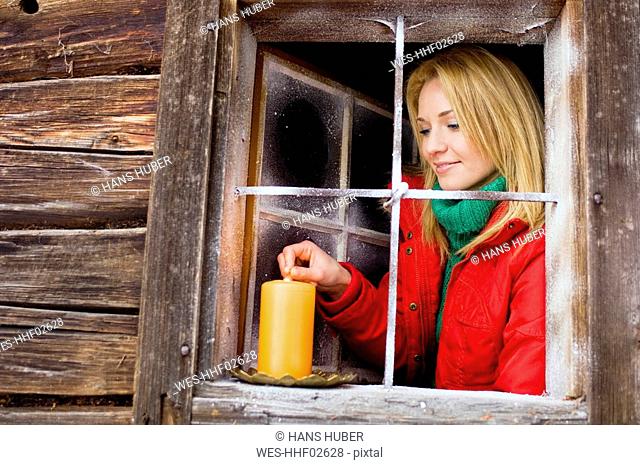 Austria, Salzburger Land, Young woman lighting candle on windowsill