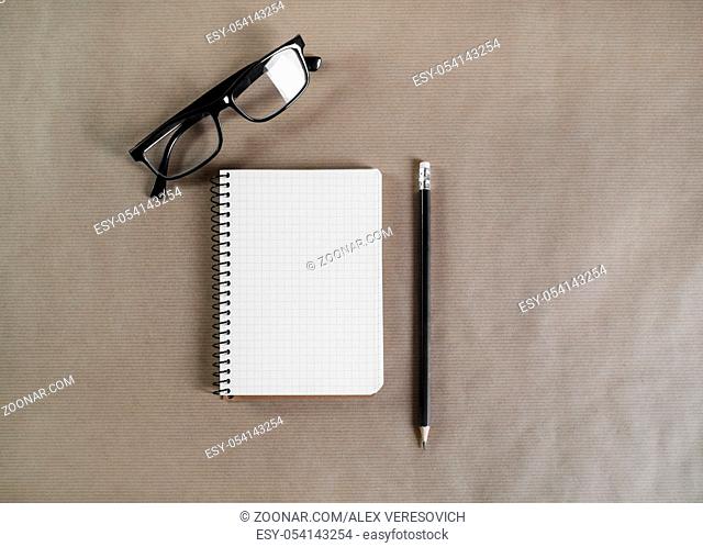Blank notepad, glasses and pencil on craft paper background. Flat lay
