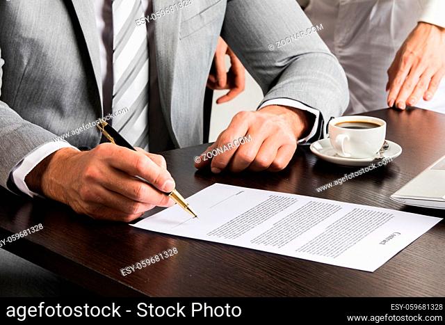 Businessman in gray suit sitting at office desk signing a contract close up