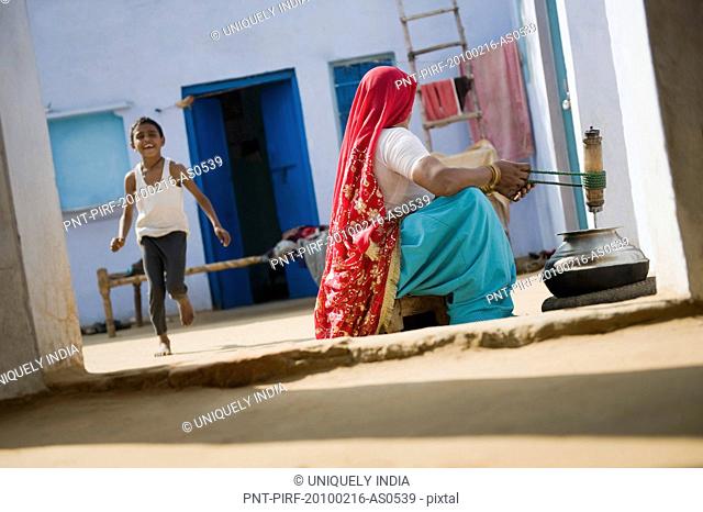 Woman churning butter with her son playing behind her, Farrukh Nagar, Gurgaon, Haryana, India