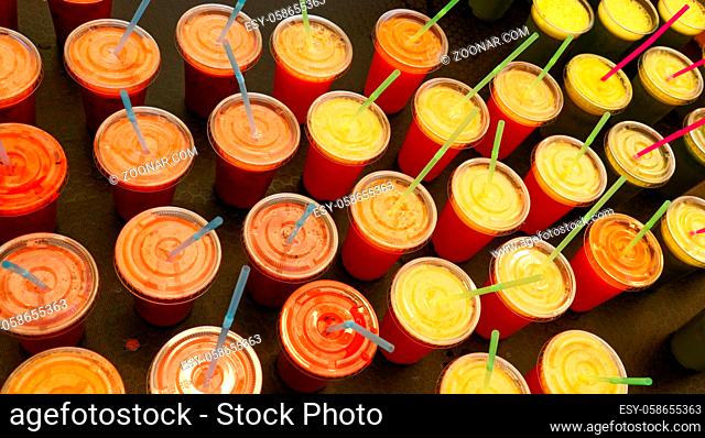 Close up many plastic glasses of fresh fruit and vegetable juices and smoothies with drinking straws at retail display, high angle view
