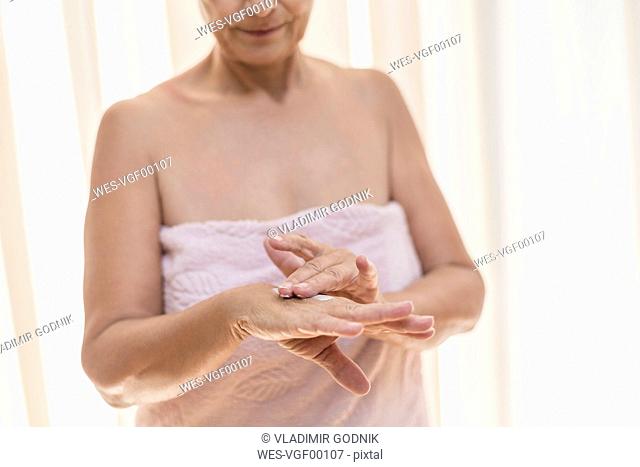 Senior woman applying cream on hand in the morning