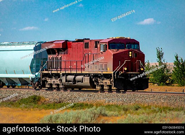 Vintage locomotive of a Canadian National Railways freight train pulling a wagon in the countryside. Painted dark red with headlights on