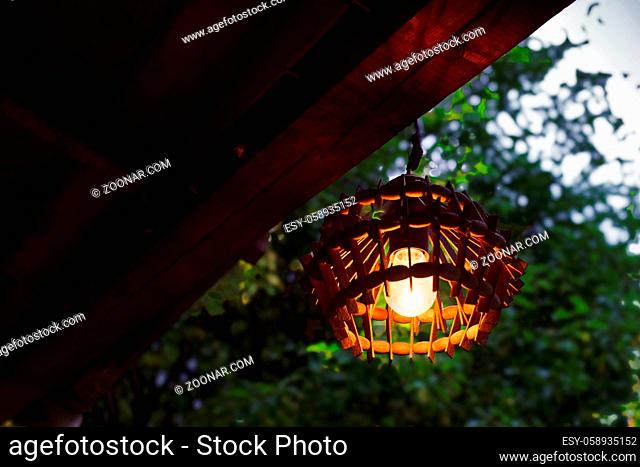 Original street lamp on the terrace of the house. Light from a light bulb in a wooden sconce. A quiet summer evening outside the city