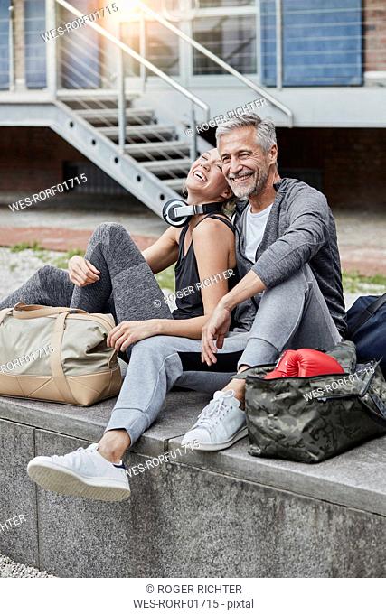 Laughing mature man and young woman with sports bag sitting in front of gym