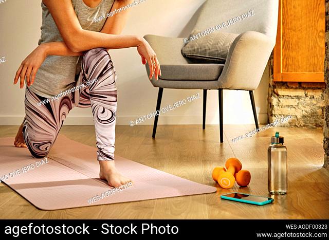 Young woman doing lunges while crouching on exercise mat at home