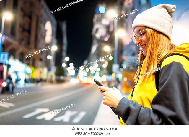 Smiling young woman in the city using her smartphone at night