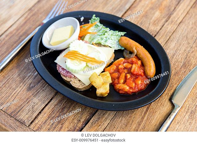cooking, asian kitchen and food concept - plate with sausage, sandwich and garnish on wooden table at restaurant