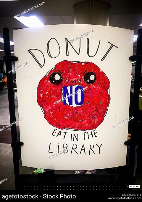 A playful sign to remind users to not bring food into the library. 'Do not' intentionally misspelled as 'Donut' with a matching pictograph, Ontario, Canada