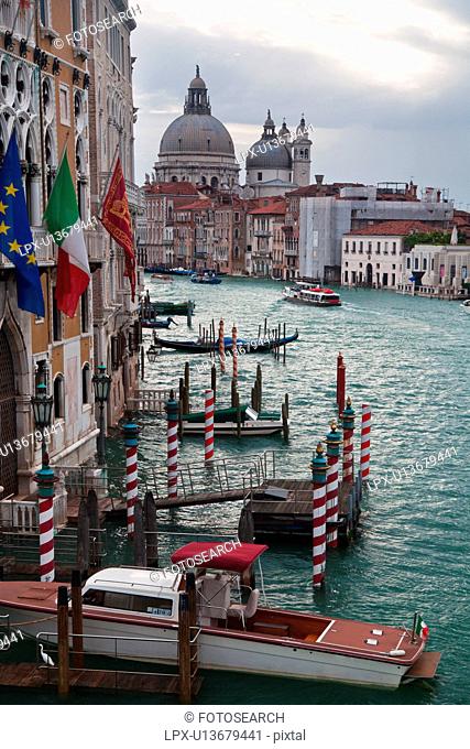 Aerial view of Grand Canal, looking towards church of Santa Maria della Salute, multicoloured flags and striped mooring posts, Venice, Northern Italy