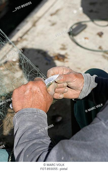 A fisherman cutting a fishing net, focus on hands