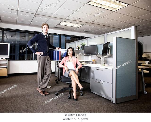 Caucasian businessman and Asian businesswoman team of people in a cubicle office space