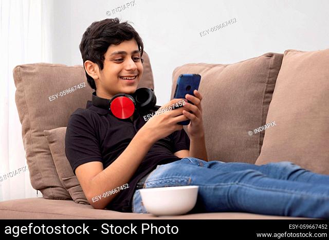 A TEENAGER SMILING AND USING MOBILE PHONE AT HOME