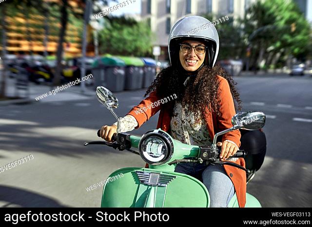 Smiling woman riding electric motor scooter in city during sunny day