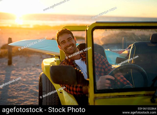Happy caucasian man sitting in beach buggy by the sea during sunset smiling