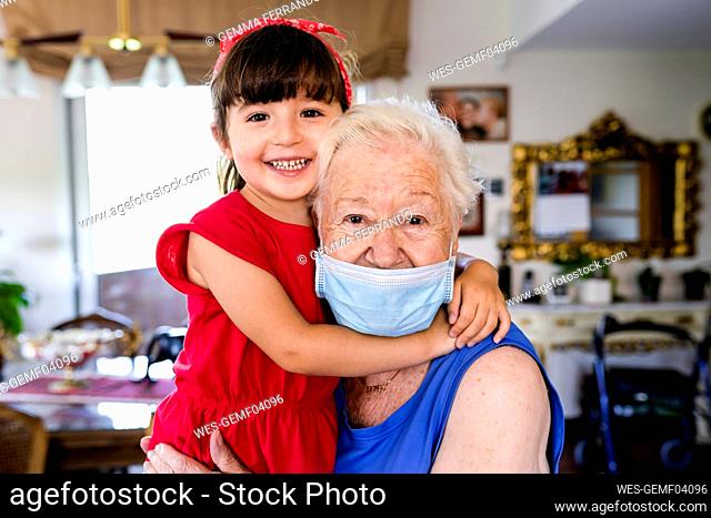 Grandmother and little girl spending family time together at home, with face mask