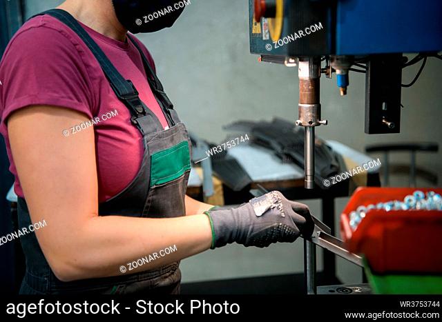 woman wearing a face mask due to coronavirus pandemic while working in the modern metal industry and using a drill. High quality photo