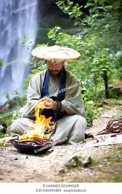 European man with beard and japanese robe makes fire ceremony in front of Great Waterfall, in Gallizien in Austria