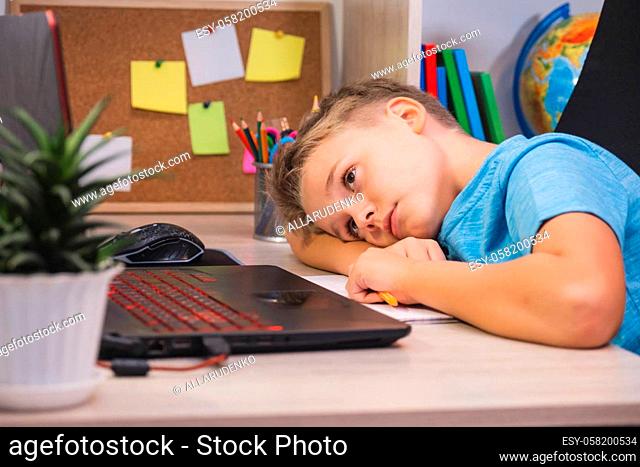 Sad schoolboy studies at home with laptop and does school homework. Home learning, online education