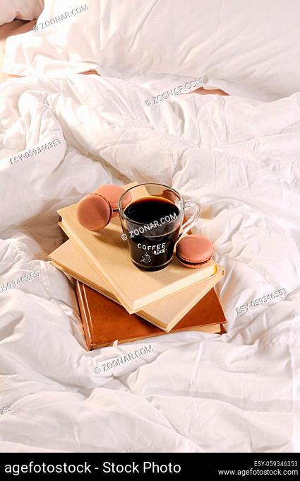 Morning cup of coffee with chocolate cakes Macaroons, on a pile of books in bed