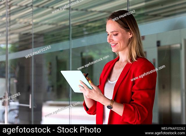Smiling female professional using digital tablet in front of glass wall