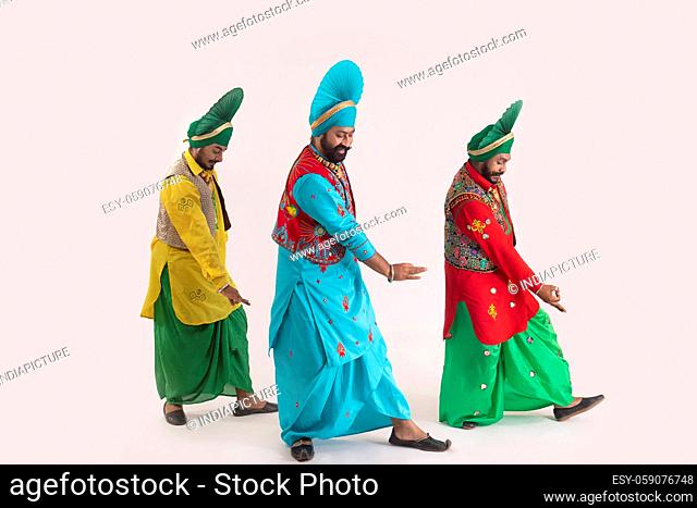 Three Bhangra dancers performing a dance step with hand gestures