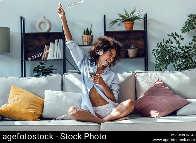 Carefree woman with hand raised sitting on sofa in living room