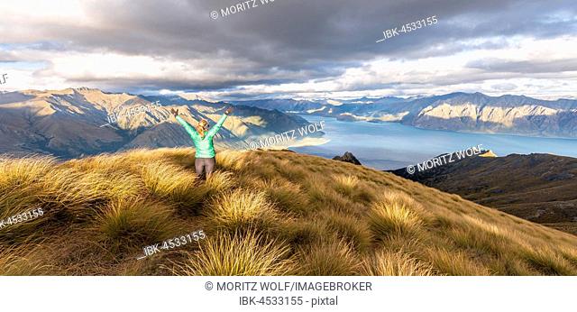 Female hiker stretching arms in the air, Lake Hawea and mountain landscape, Isthmus Peak, Otago, South Island, New Zealand
