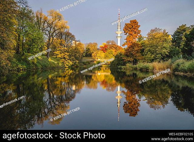 Germany, Hamburg, Autumn trees reflecting on surface of shiny lake in Wallanlagen park
